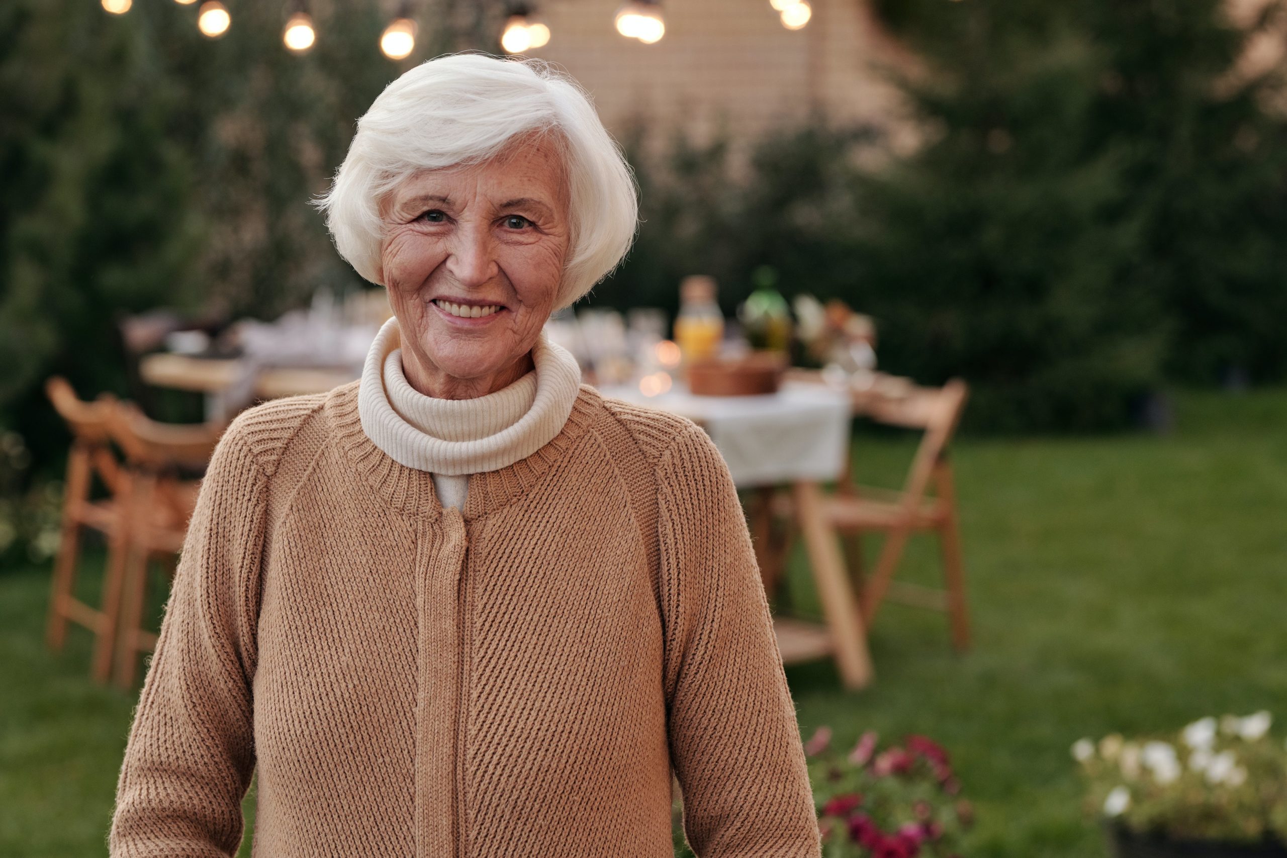 Eldre kvinne står i hagen sin foran et dekket bord til gjester