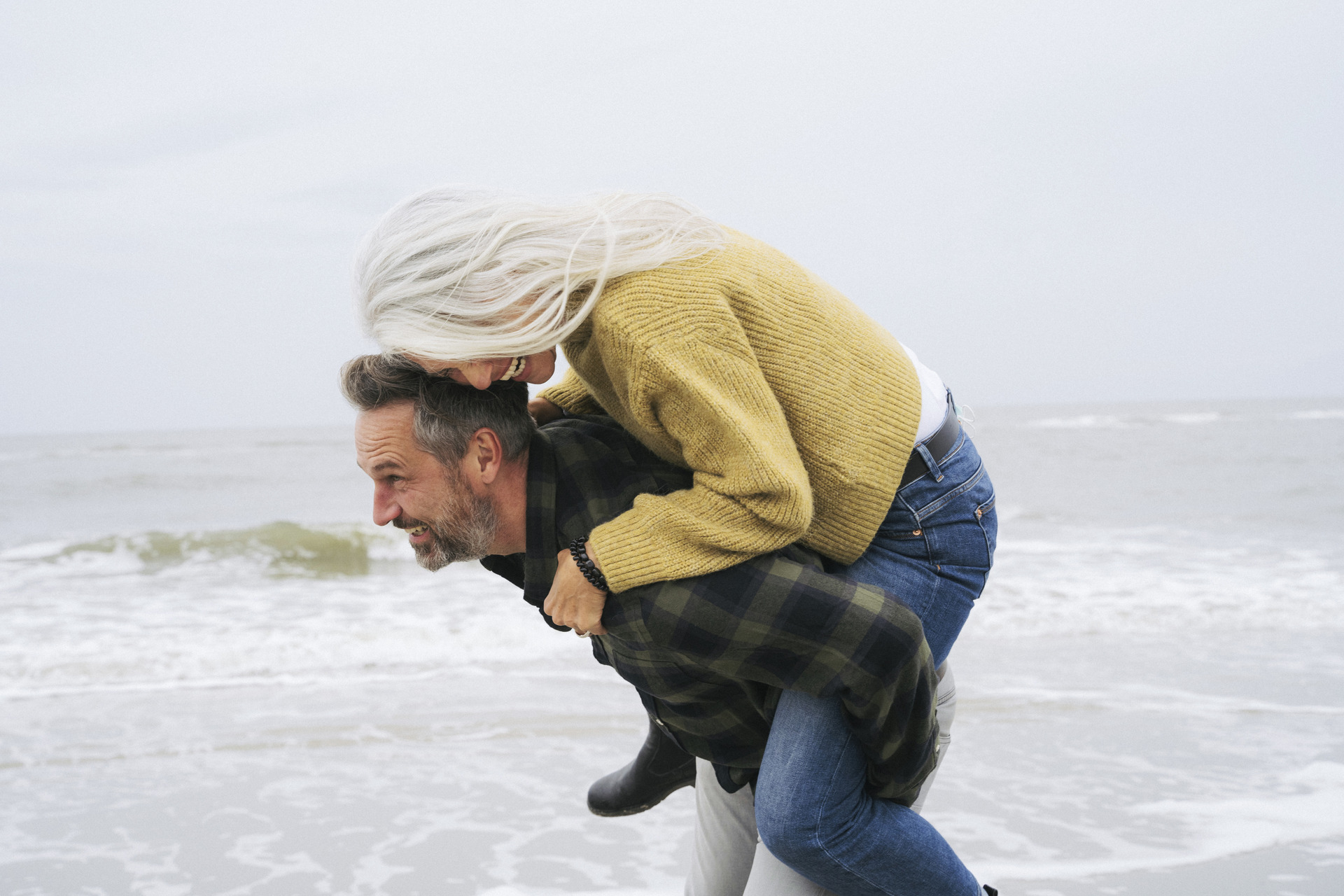 Mann på strand løper med en kvinne som han bærer på ryggen