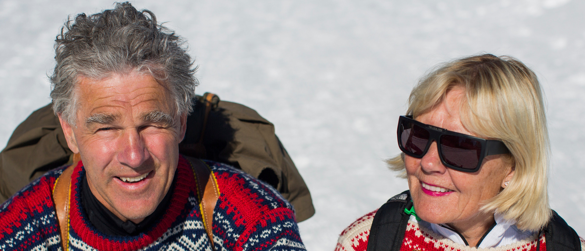 Et eldre ektepar i sterk sol sitter med Mariusgensere etter en skitur